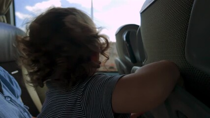 Toddler seated on lap opens and explores plastic tray table on back of bus seat during journey, engaging in playful tactile discovery while traveling