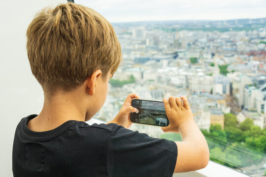 Young boy taking picture with a smartphone of London cityscape from skyscraper window