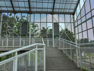 modern architectural walkway with a metal grid railing, showing the transition from an indoor glass...