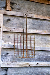 This is an image of a rusted metal object which appears to be a piece of farm equipment or a tool hanging on a wooden wall
