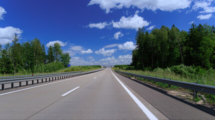 Fototapeta premium Road view on a summer day. Highways and cars, roadside and white road line markings.