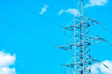 Tall electric transmission tower against a bright blue sky with scattered clouds during the day
