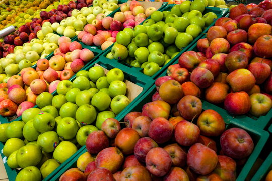 Fresh apples in various colors displayed in baskets at a fruit market during the afternoon, showcasing the diversity of apples
