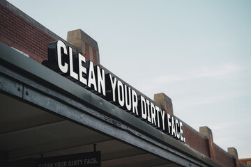 Obraz premium Clean Your Dirty Face Sign on Top of Building in Historic City With Cloudy Sky