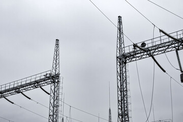 Power transmission structures under a cloudy sky near an energy facility during winter with overhead lines and machinery visible