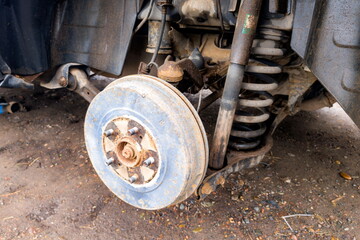 Detailed view of a car's wheel assembly showing the brake drum, suspension, and surrounding components in a mechanic's workshop during daylight
