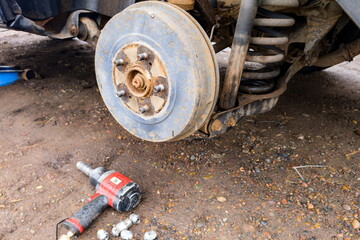 Car brake system exposed during maintenance with tools and parts scattered on the ground at a...