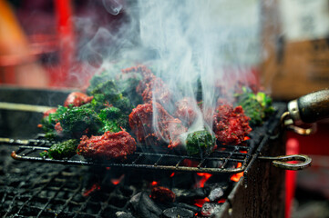 Smokey chicken 65 grilled on metallic net at vendor.