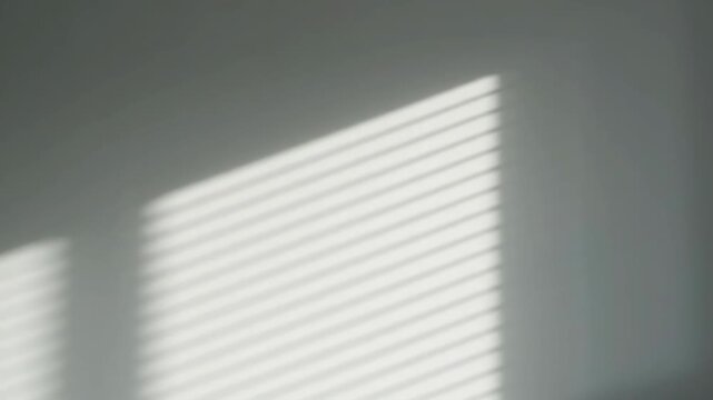 Sunlight Stripes on Wall - Soft sunlight filters through window blinds, casting delicate, parallel stripes of light and shadow onto a light gray wall.