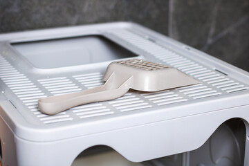 A cat litter box that features a scoop resting on top of it