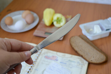 Close-up of a hand turning a page in a vintage recipe book, with bread and eggs nearby. Perfect for culinary blogs, cookbook illustrations, and food-related marketing.