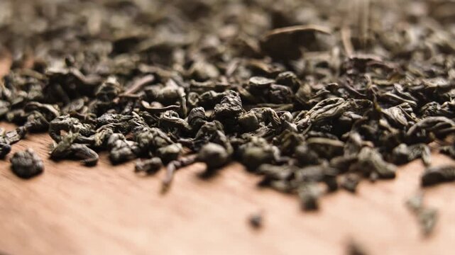 Falling dried curled leaves of chinese traditional green tea on wooden table. Organic beverage aromatic ingredient. Macro. Slow motion. Rotation