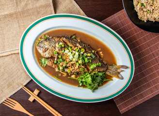 Whole Fried Fish with Garlic Sauce and Fresh Herbs on Oval Plate, Top View of Authentic Asian Seafood Dish
