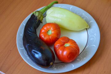 fresh vegetables eggplant two red tomatoes pale yellow bell pepper arranged decorative white plate wooden table healthy eating fresh vegetarian cooking farm-to-table concept