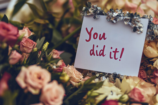 A close-up view features a colorful bouquet of flowers accompanied by a handwritten note expressing congratulations. The note, placed prominently, adds a personal touch