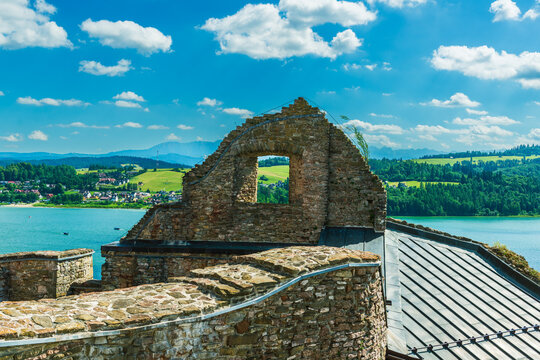 Weathered brick and stone wall of Czorsztyn Castle with an arched window opening to green hills and a blue sky in the distance. The medieval fortress remains highlight Polish heritage and history, sur - Powered by Adobe