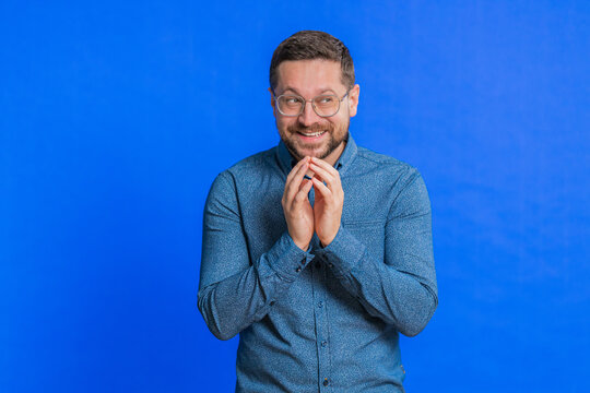 Sneaky cunning Caucasian middle-aged man in glasses with tricky face gesticulating and scheming evil plan, thinking over devious villain idea, cheats, jokes, pranks. Guy isolated on blue background