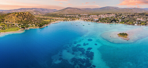 Amazing sunset seascape with boats floating on calm crystal clear turquoise water near coastline with green hills and mountains in the background