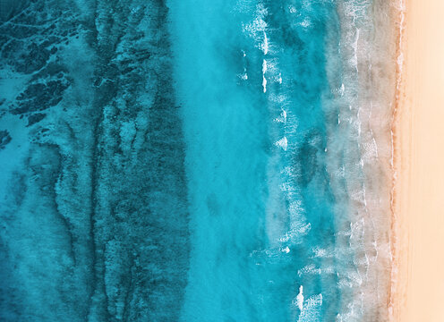 Aerial view of turquoise water gently washing golden sand on a tropical beach creating a beautiful contrast of colors