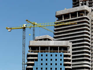 Construction cranes over high rise building with concrete framework and glass elements in