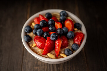 Oatmeal with ripe strawberries, blueberries and honey in the bowl. Selective focus.