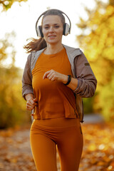 Hello autumn. trendy middle aged woman in fitness clothes in the park with headphones running.