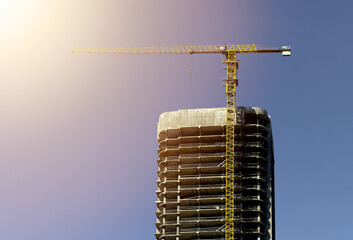 Skyscraper under construction with steel crane and glass facade in warm golden hour sunlight. Modern
