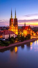 Fototapeta premium Illuminated cathedral and city buildings reflected in a tranquil river at dusk.