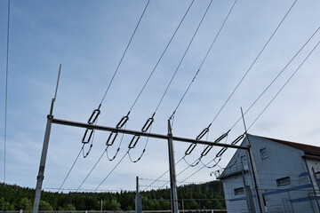 Close-up of high voltage electrical power lines with insulators above a substation building,...