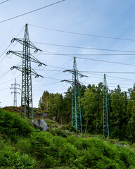 Tall steel power pylons with high voltage cables crossing a lush green hillside and forest under a...