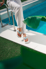 A woman dressed in stylish white pants along with trendy brown sandals is standing elegantly next...