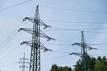 Steel lattice power line towers with high voltage cables against a bright blue summer sky, forest...