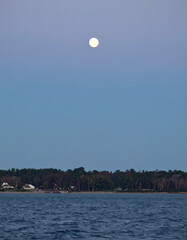 Full moon over calm water and shoreline