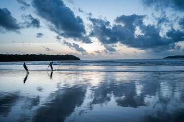 Dusk at Caranzalem Beach, Goa, with dramatic cloudy skies, waves, and two backlit cliffs. Two...