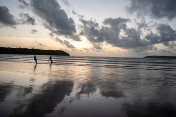 Dusk at Caranzalem Beach, Goa, with dramatic cloudy skies, waves, and two backlit cliffs. Two...