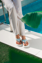 A woman who is wearing flip flops is standing right next to a pool
