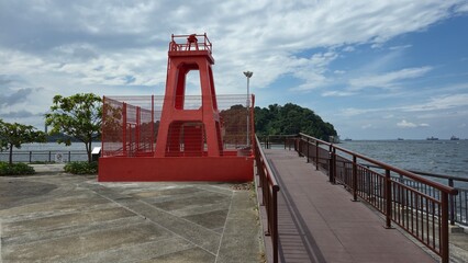 Singapore - 5 July 2025. Red lighthouse near boardwalk with ocean view and distant island.