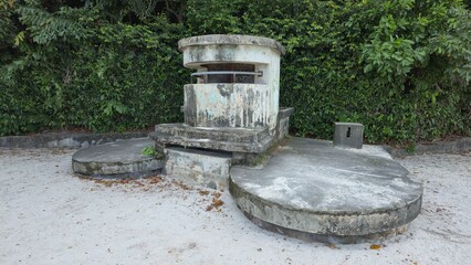 Singapore - 5 July 2025. Circular World War II pillbox on beach sand with lush vegetation in...