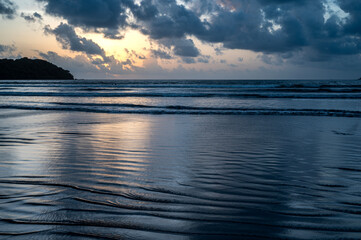 View of the Arabian Sea from Miramar Beach, Goa, at dusk after sunset, with grey clouds, orange glow in the sky, low waves, and backlit cliffs creating a serene monsoon coastal scene.