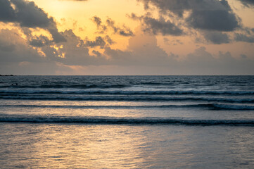 Sunset view of Vagator Beach Goa with Arabian Sea, golden yellow sky, dramatic grey monsoon clouds, and shimmering water reflecting the sun’s warm light in the evening.