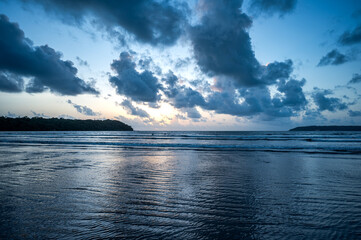 View of the Arabian Sea from Miramar Beach, Goa, at dusk after sunset, with grey clouds, orange glow in the sky, low waves, and backlit cliffs creating a serene monsoon coastal scene.