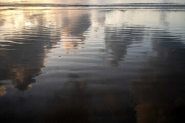 Reflection of monsoon sunset at Miramar Beach Panjim Goa on wet sand, showing Arabian Sea hues,...