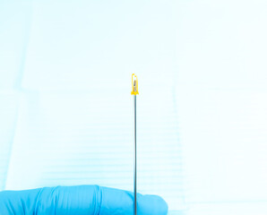 Close-up of a 14G IV cannula needle with yellow safety mechanism, held by a blue nitrile gloved hand against a light blue sterile background, used for safe venous access.