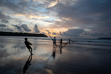 Fishermen casting fishing nets at Miramar Beach, Panjim, Goa during a monsoon evening, with waves,...