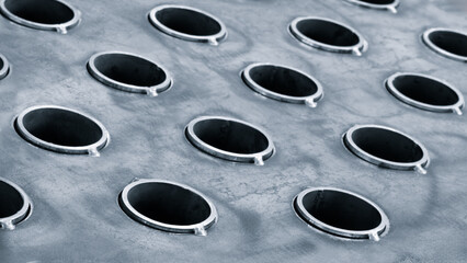 Close up of a metal surface with many small holes. holes are all the same size and shape, and they are all lined up in a row. surface appears to be made of metal