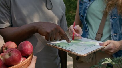 Medium shot of hands and midsection of unrecognizable diverse volunteers standing in community park, studying garden plan and discussing planting of flowers - Powered by Adobe