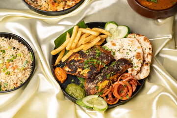 Indian tawa masala fish on banana leaf with fries, salad, chutney, kulcha breads, and rice, served in black plate over vibrant yellow satin background.