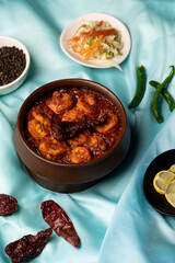 Prawn Balchão Brioche with aged cheddar and sesame seeds, styled on a blue satin background with lemon slices, raw green chillies, black pepper, and dried red chilli.