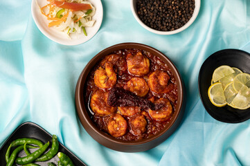 Prawn Balchão Brioche with aged cheddar and sesame seeds, styled on a blue satin background with lemon slices, raw green chillies, black pepper, and dried red chilli.