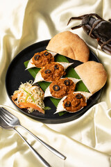 Stuffed crabs served on a banana leaf with salad and Goan poi, styled on a black plate on yellow satin background with spoon, fork, and raw crab.
